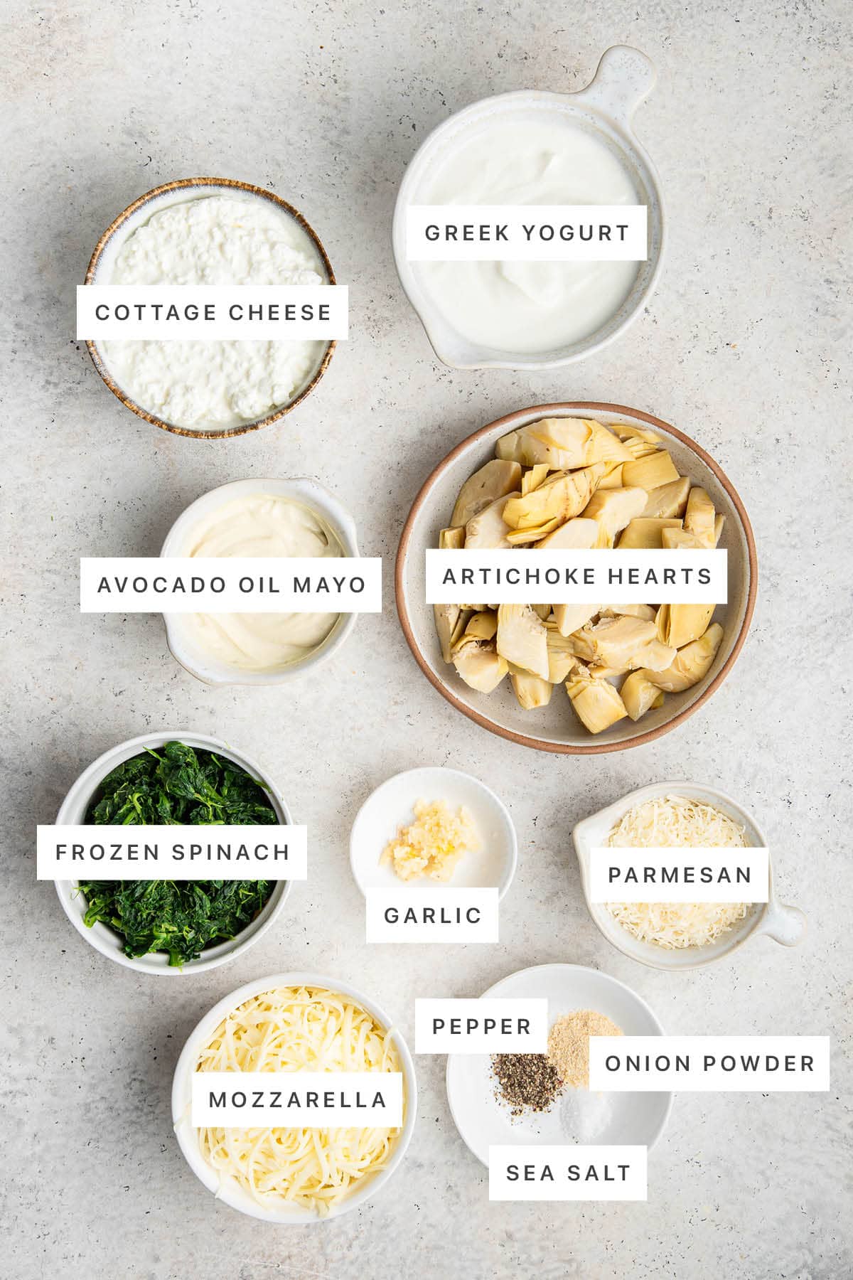 Ingredients measured out to make Healthy Spinach Artichoke Dip: cottage cheese, Greek yogurt, avocado oil mayo, artichoke hearts, frozen spinach, garlic, parmesan, mozzarella, pepper, sea salt and onion powder.