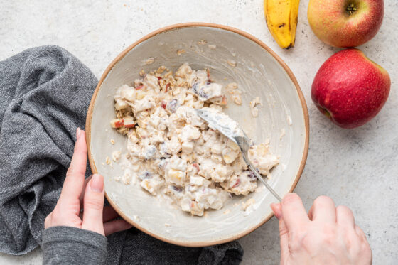 Woman mixing bircher muesli in a bowl with a large spoon.