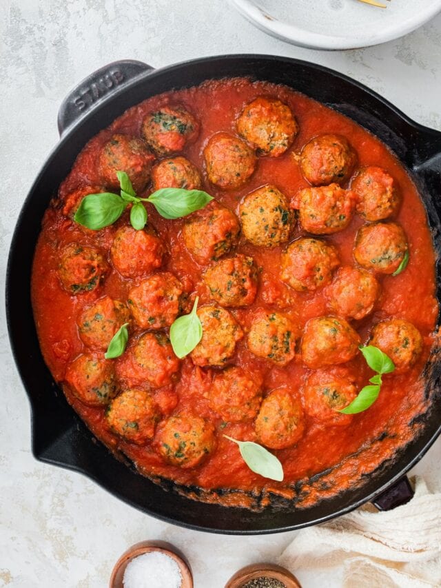 Spinach turkey meatballs with pasta sauce in a cast iron skillet.