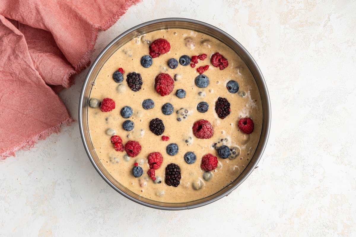 Berry cake batter poured into a springform pan, topped with more berries.