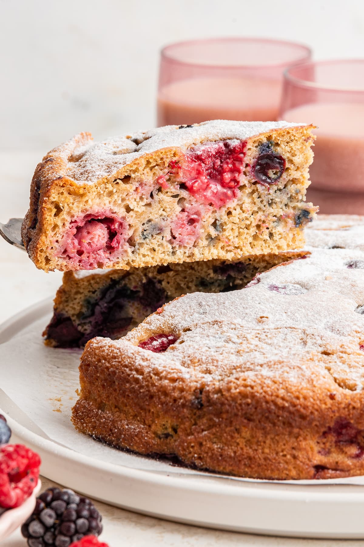A silver spatula removing a slice of easy berry cake from a white plate.