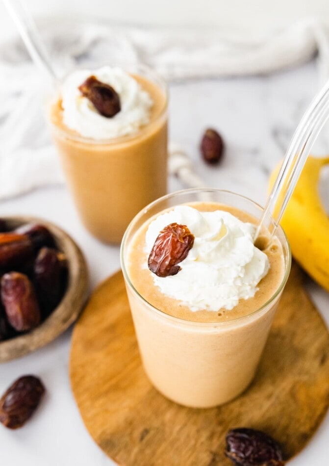 This healthy date shake is made with frozen bananas instead of ice cream and requires only four simple ingredients. It's dairy-free, gluten-free and vegan. Two healthy date shakes topped with whipped cream and a date.