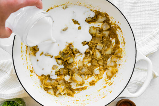 Pouring coconut milk into pot of veggies and seasonings.