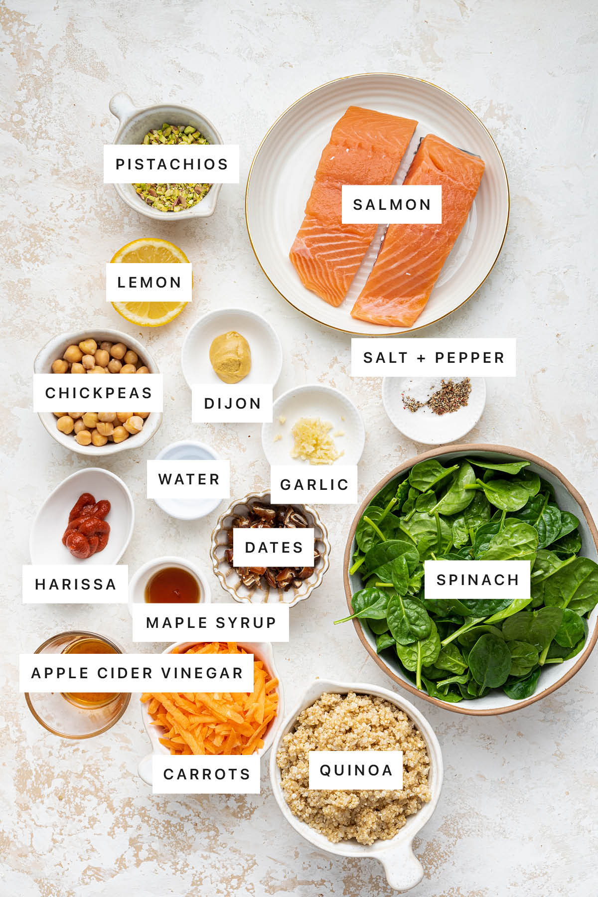 Ingredients measured out to make Pistachio Salmon Salad with Spicy Harissa Dressing: pistachios, salmon, lemon, dijon, chickpeas, salt, pepper, water, garlic, harissa, dates, spinach, maple syrup, vinegar, carrots and quinoa.