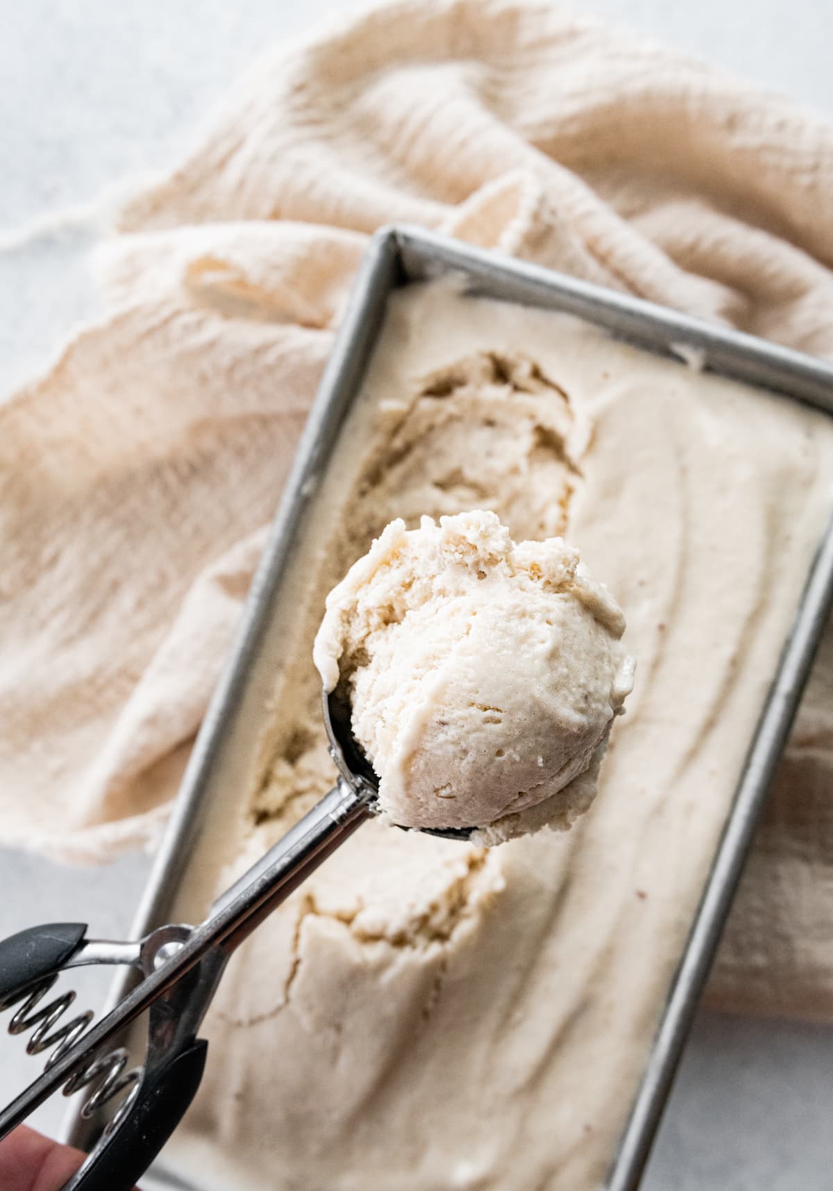 Woman's hand holding ice cream scooper that scooped banana frozen yogurt from a loaf pan.