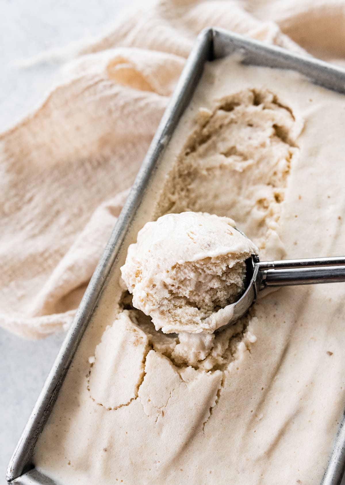 Ice cream scooper scooping banana frozen yogurt from loaf pan.