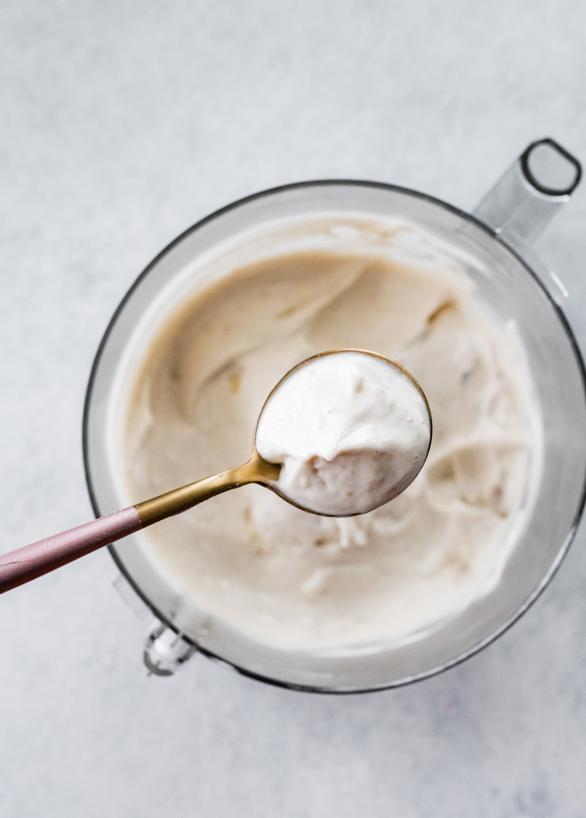 Small spoon scooping a bite of banana frozen yogurt from a food processor.