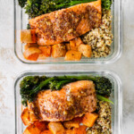 Two glass storage containers with a bed of quinoa topped with roasted sweet potatoes and broccolini and mustard maple salmon.