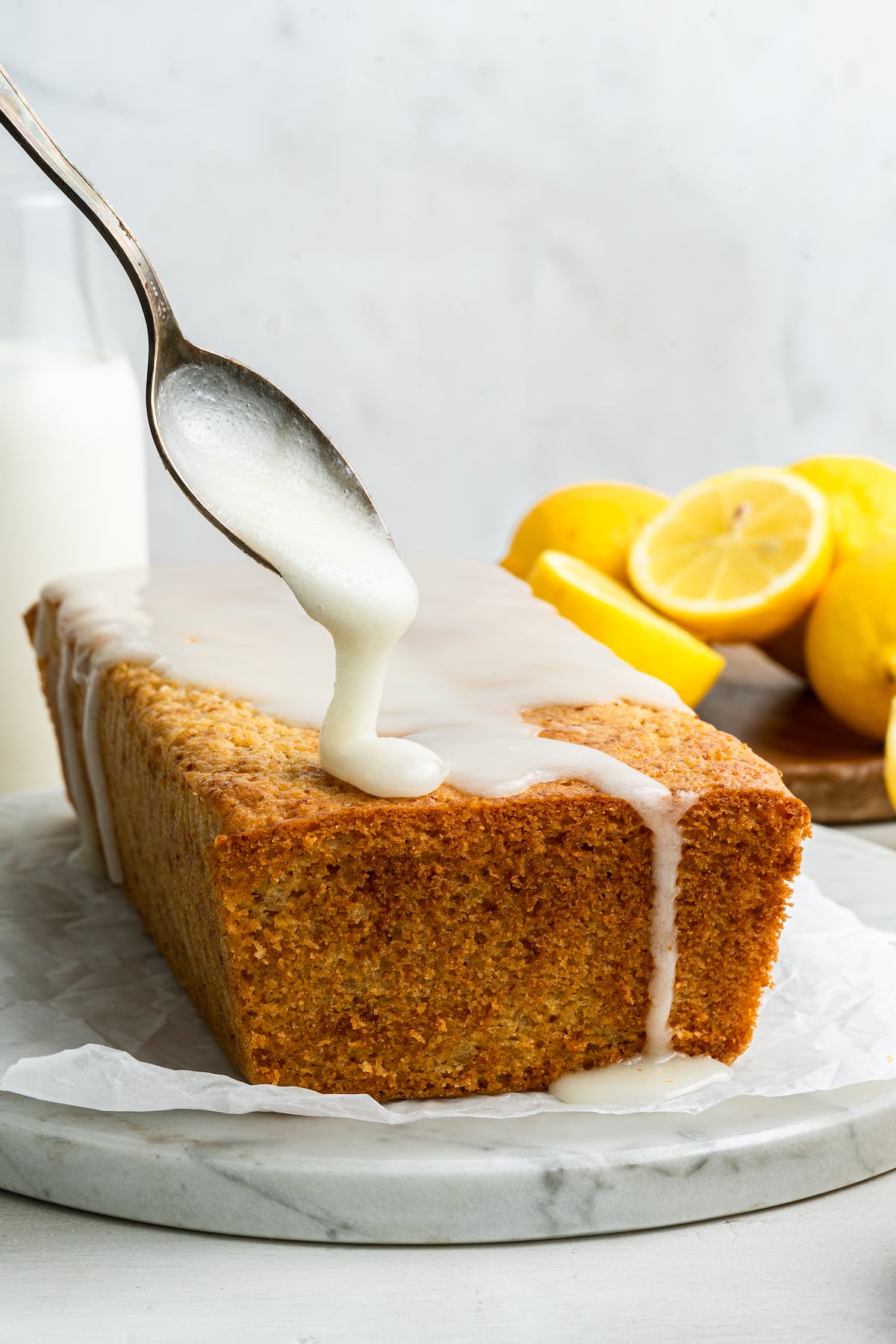 Spoon drizzling a lemon glaze over a lemon loaf.
