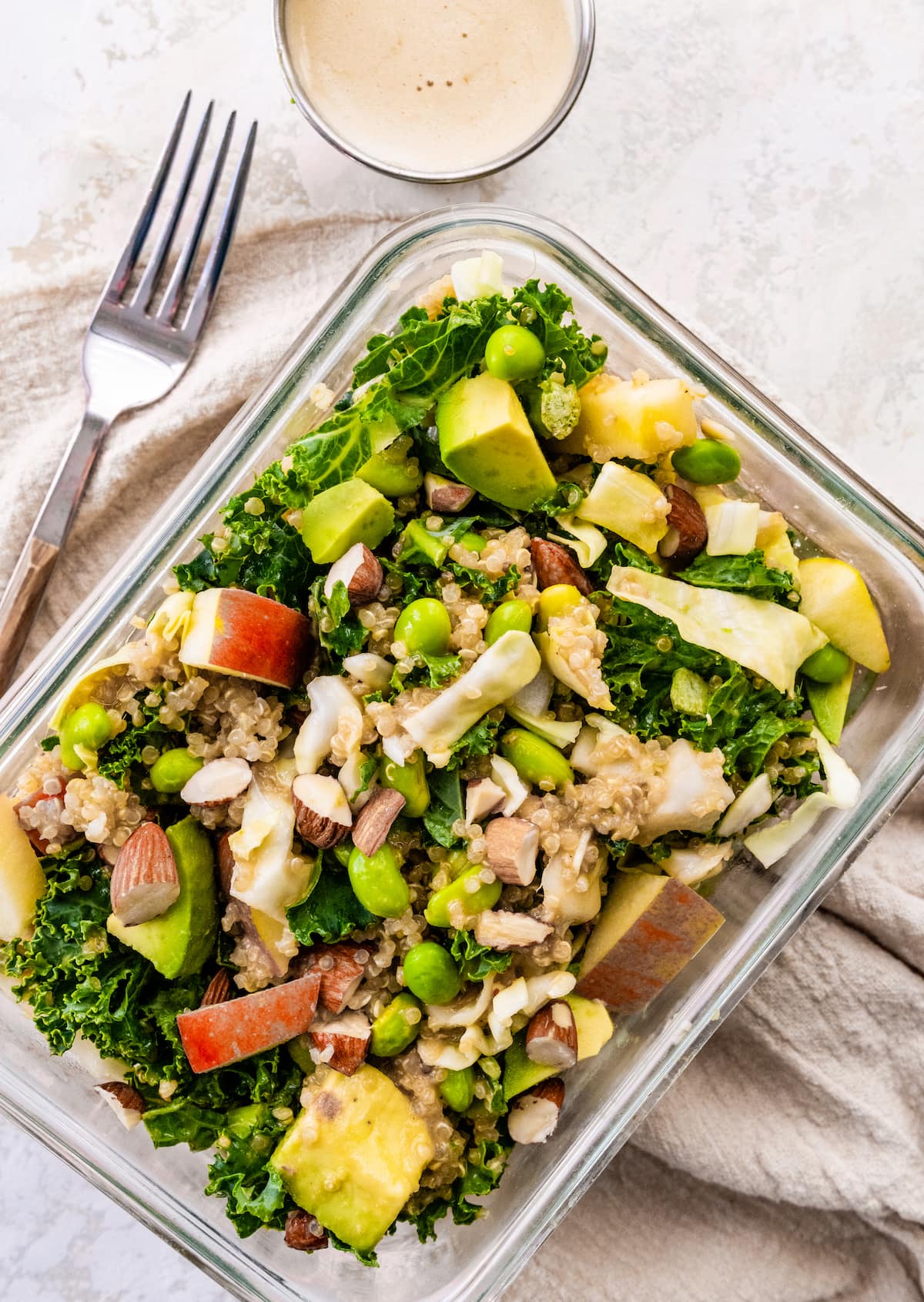 One glass storage container with a combined meal prep detox salad, served with a fork and a side of dressing.