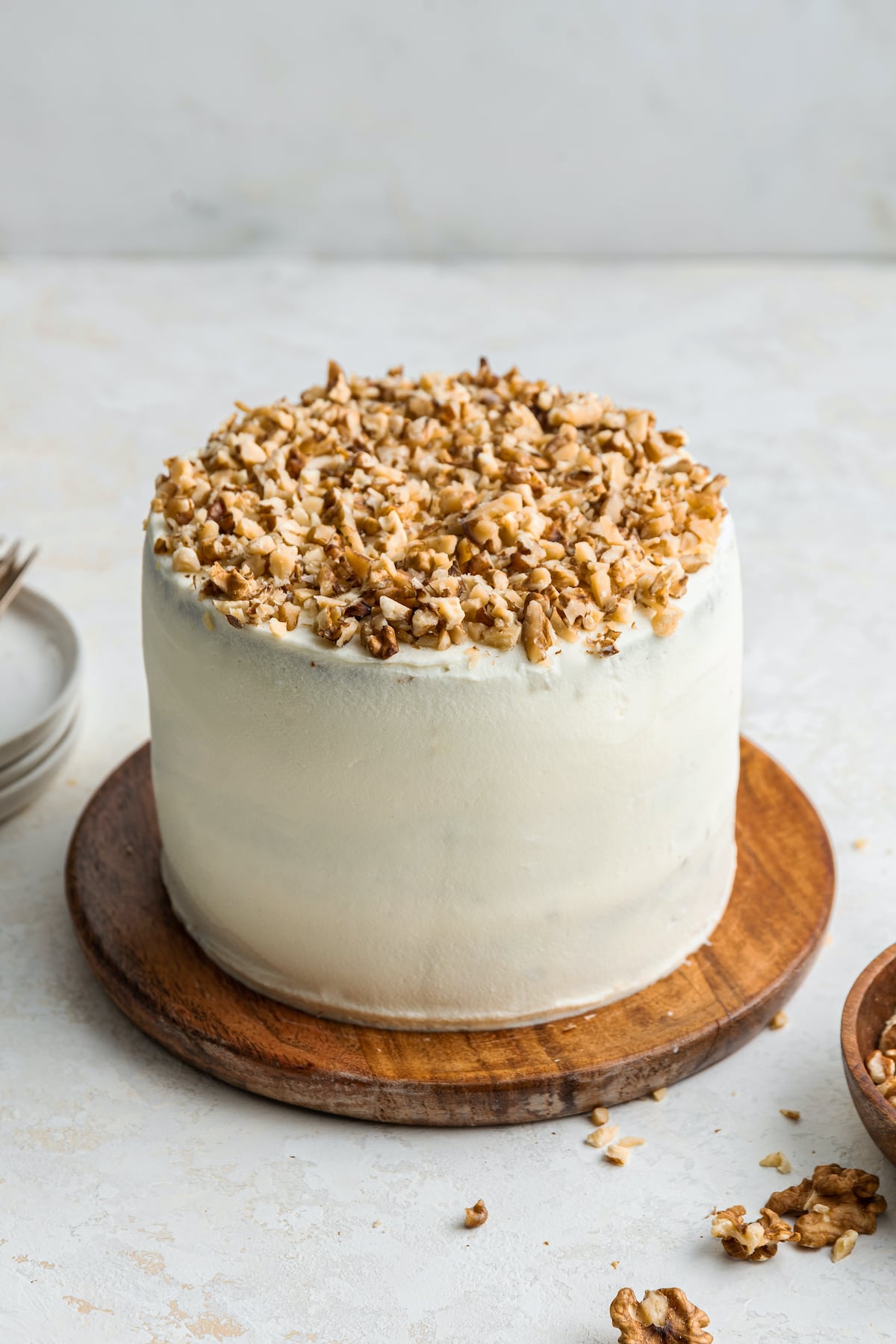 A fully frosted 3-layer oatmeal carrot cake topped with chopped walnuts and served on a wooden board.