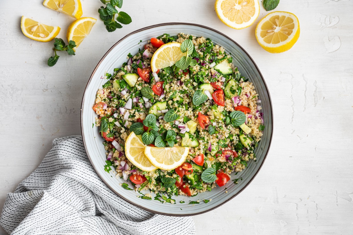 Quinoa tabbouleh all mixed together in a serving bowl, topped with fresh lemon slices and fresh herbs.