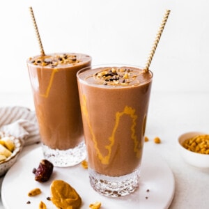 Two snickers protein smoothies with drizzle of peanut butter inside glasses.