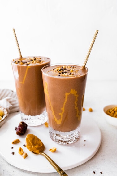 Two snickers protein smoothies with drizzle of peanut butter inside glasses.