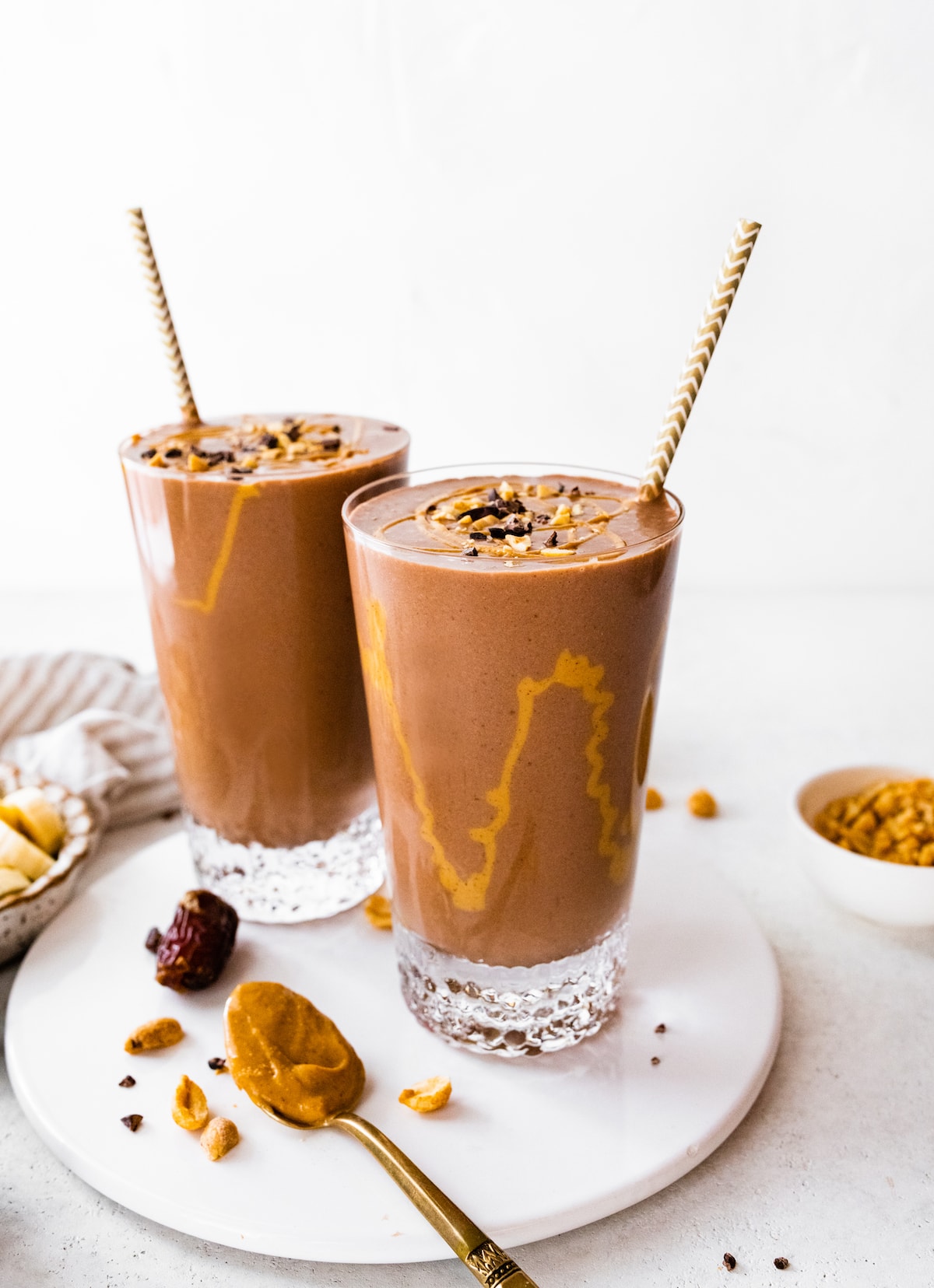 Two snickers protein smoothies with drizzle of peanut butter inside glasses.