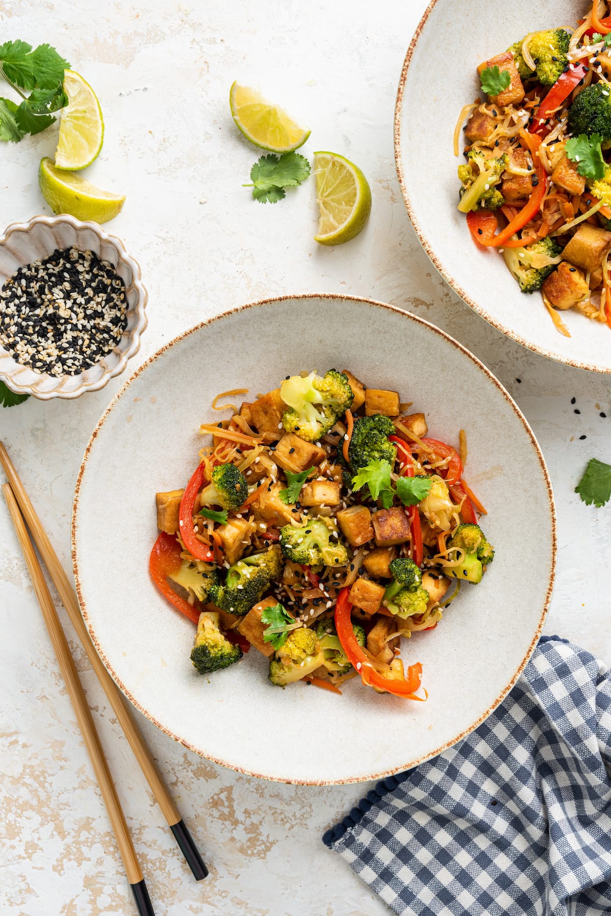 Tofu Veggie Noodle Bowl with Cabbage Noodles with Sriracha Two tofu cabbage noodle bowls with chopsticks next to one bowl and fresh lime wedges scatted around bowls.