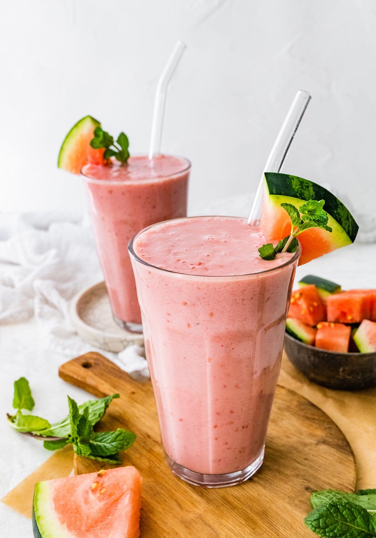 Two watermelon smoothies with straws and fresh watermelon slices.