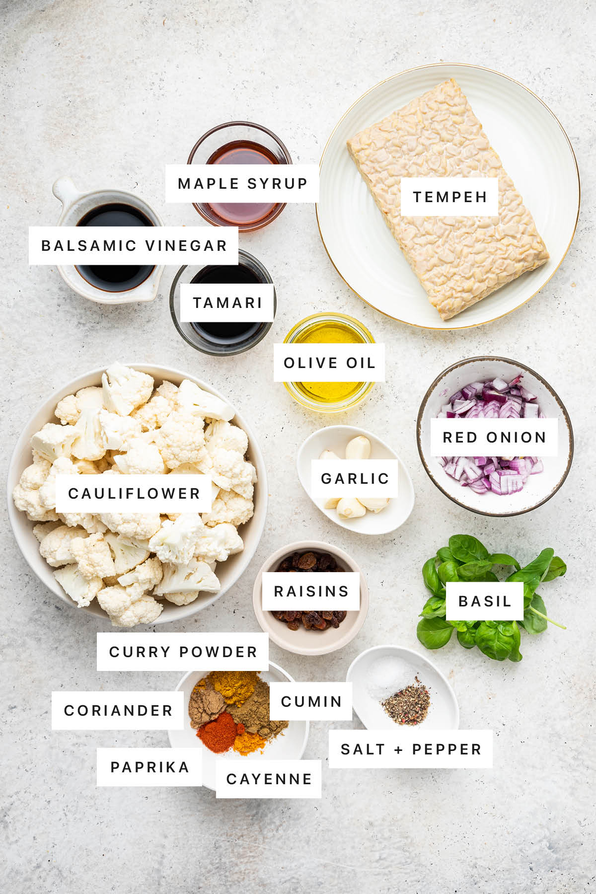 Ingredients measured out to make Curried Cauliflower and Tempeh Bowl: maple syrup, balsamic vinegar, tamari, olive oil, tempeh, red onion, garlic, cauliflower, raisins, basil, curry powder, coriander, cumin, paprika, cayenne, salt and pepper.