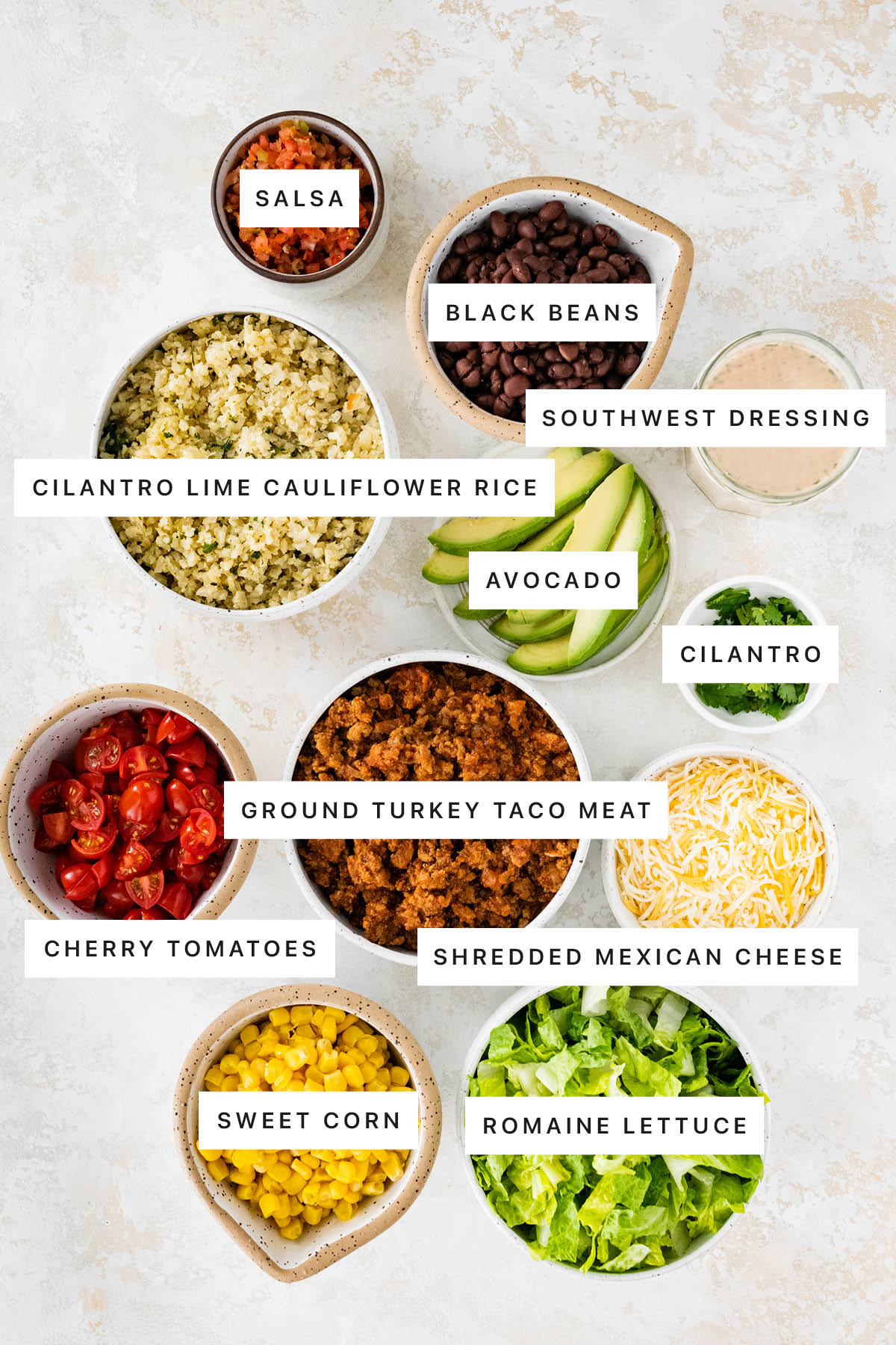 Ingredients measured out to make Turkey Taco Meal Prep Bowls: salsa, black beans, southwest dressing, cilantro lime cauliflower rice, avocado, cilantro, ground turkey taco meat, cherry tomatoes, shredded Mexican cheese, sweet corn and romaine lettuce.