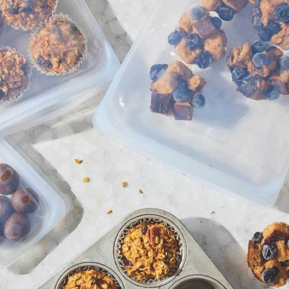 Three plastic packets filled with bit sized snacks and muffins and a muffin tin near with baked muffins inside.