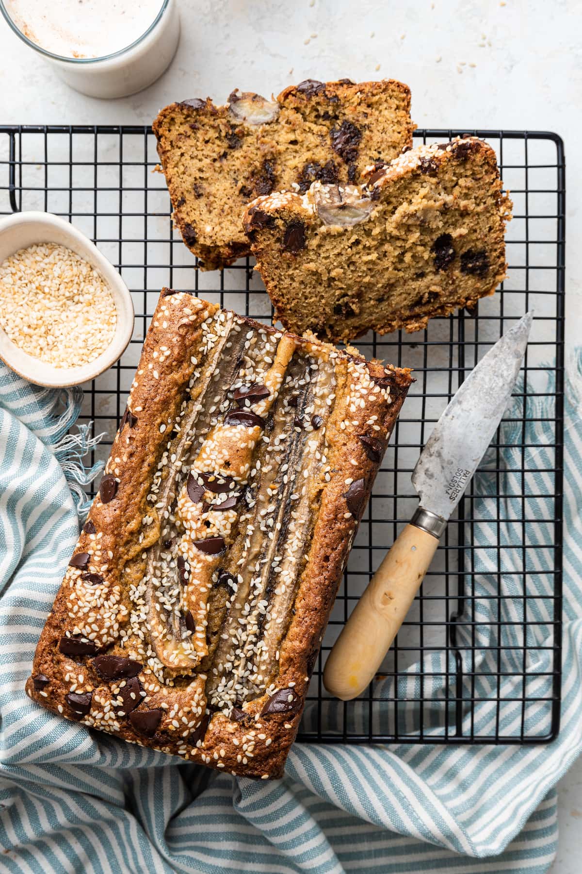A top view of the loaf of tahini banana bread with two slices and a knife on a wire rack.