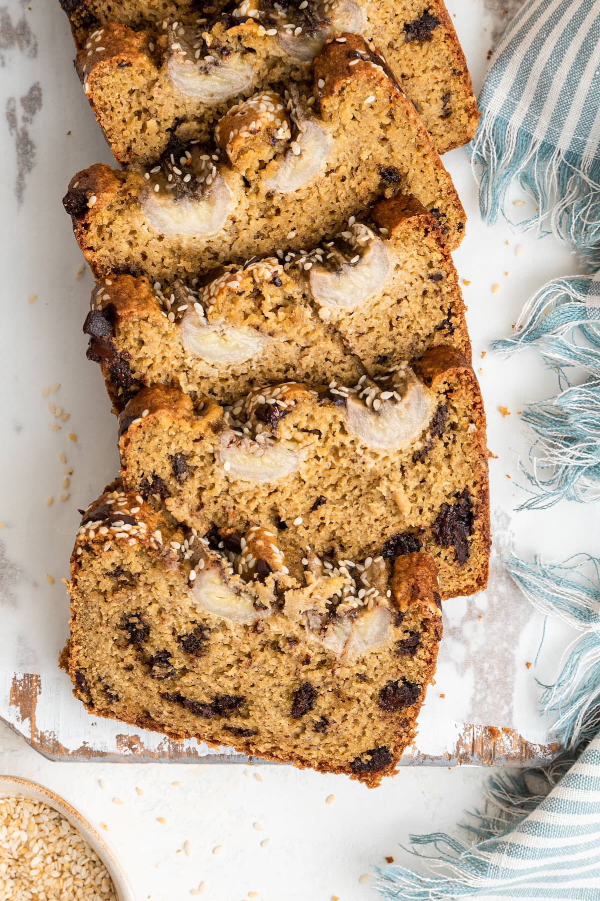 Five slices of tahini banana bread rest on one another on a cutting board.