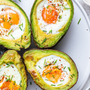 Four avocado halves with a baked egg in the center of each, topped with fresh chives, and spices.