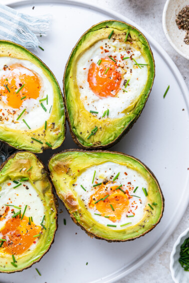 Four avocado halves with a baked egg in the center of each, topped with fresh chives, and spices.