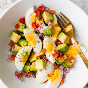 A serving of hard boiled eggs with avocado, red onion, red bell pepper, and topped with ground pepper.