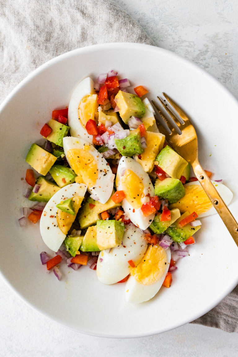 A serving of hard boiled eggs with avocado, red onion, red bell pepper, and topped with ground pepper.