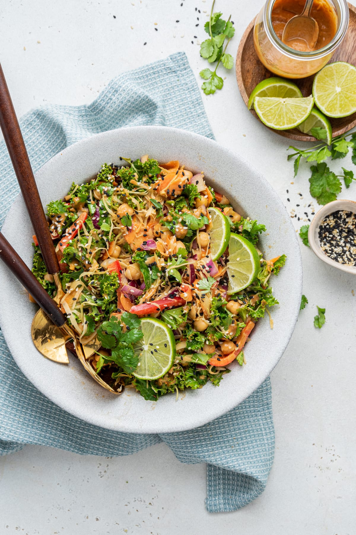 Kale and cabbage pad Thai salad being served in a bowl with two metal serving spoons.