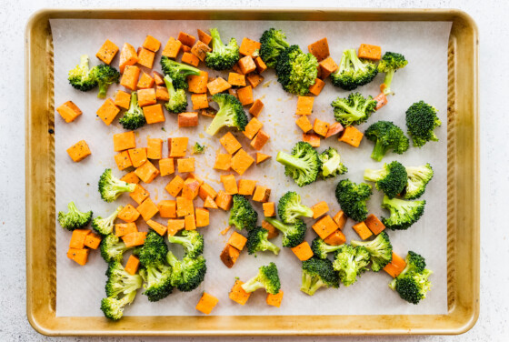 A baking tray with diced sweet potato and broccoli florets before being roasted.