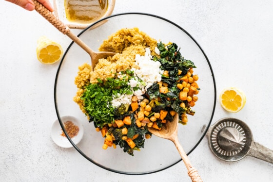 Two serving spoons mixing the roasted broccoli quinoa salad in a large glass bowl.