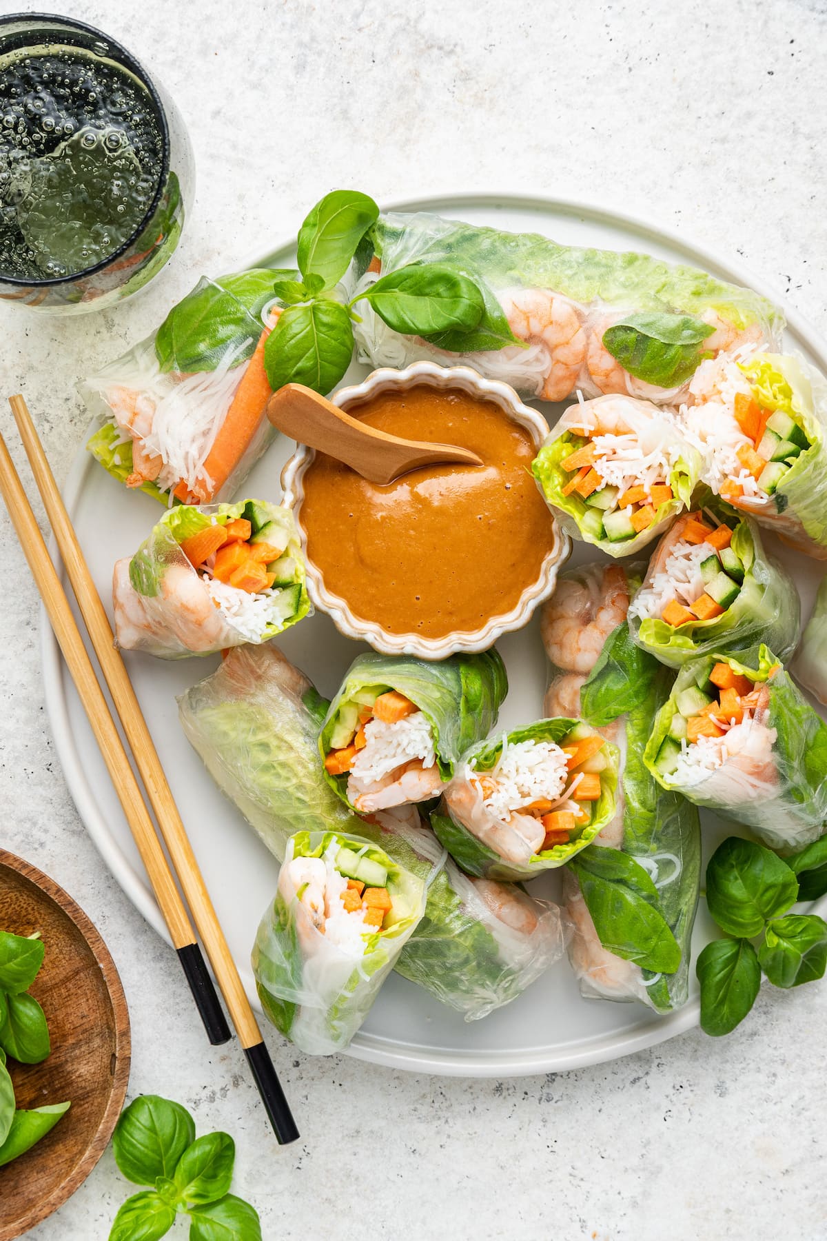 A large plate with shrimp spring rolls, wooden chopsticks, and a small bowl of peanut sauce.