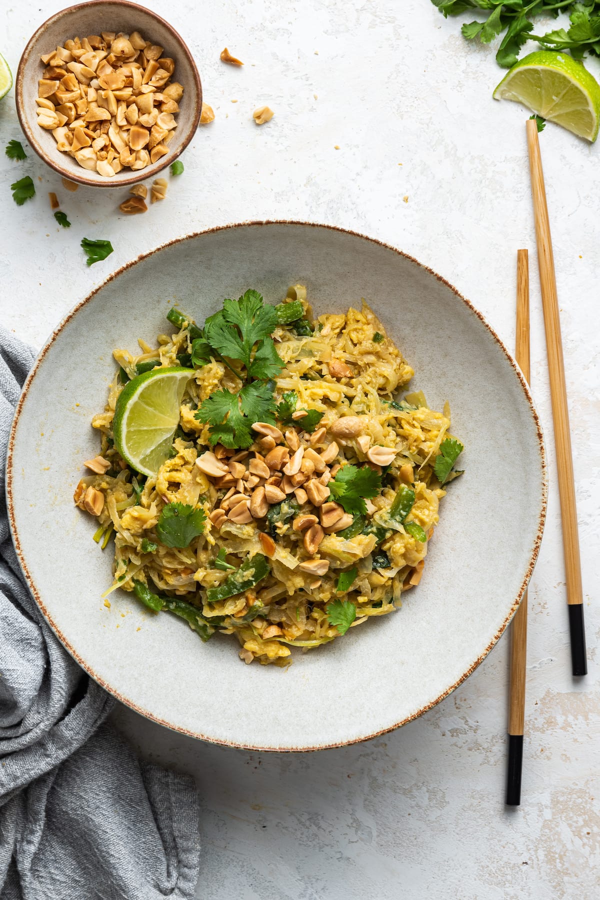HEALTHY Pad Thai with Cabbage Noodles (low carb + gluten-free) Healthy pad thai garnished with fresh cilantro and peanuts on a white plate with wooden chopsticks.