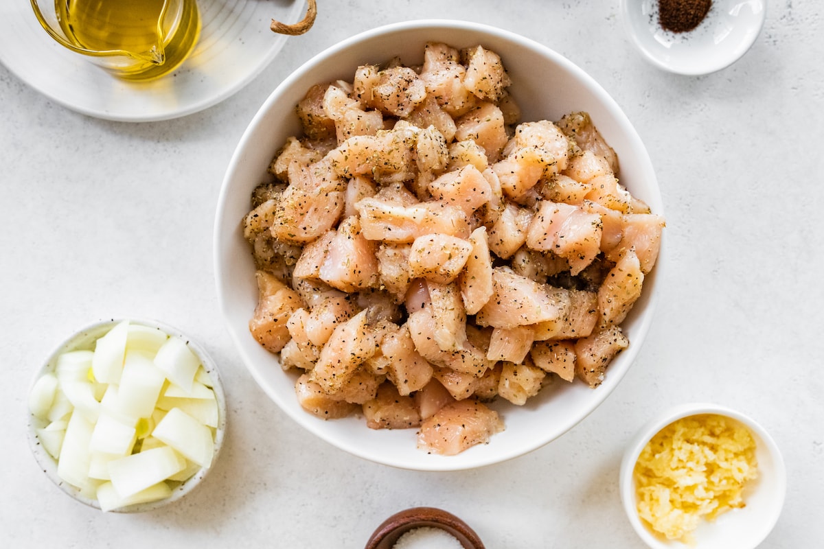 Raw chicken with herbs and spices in a white bowl.