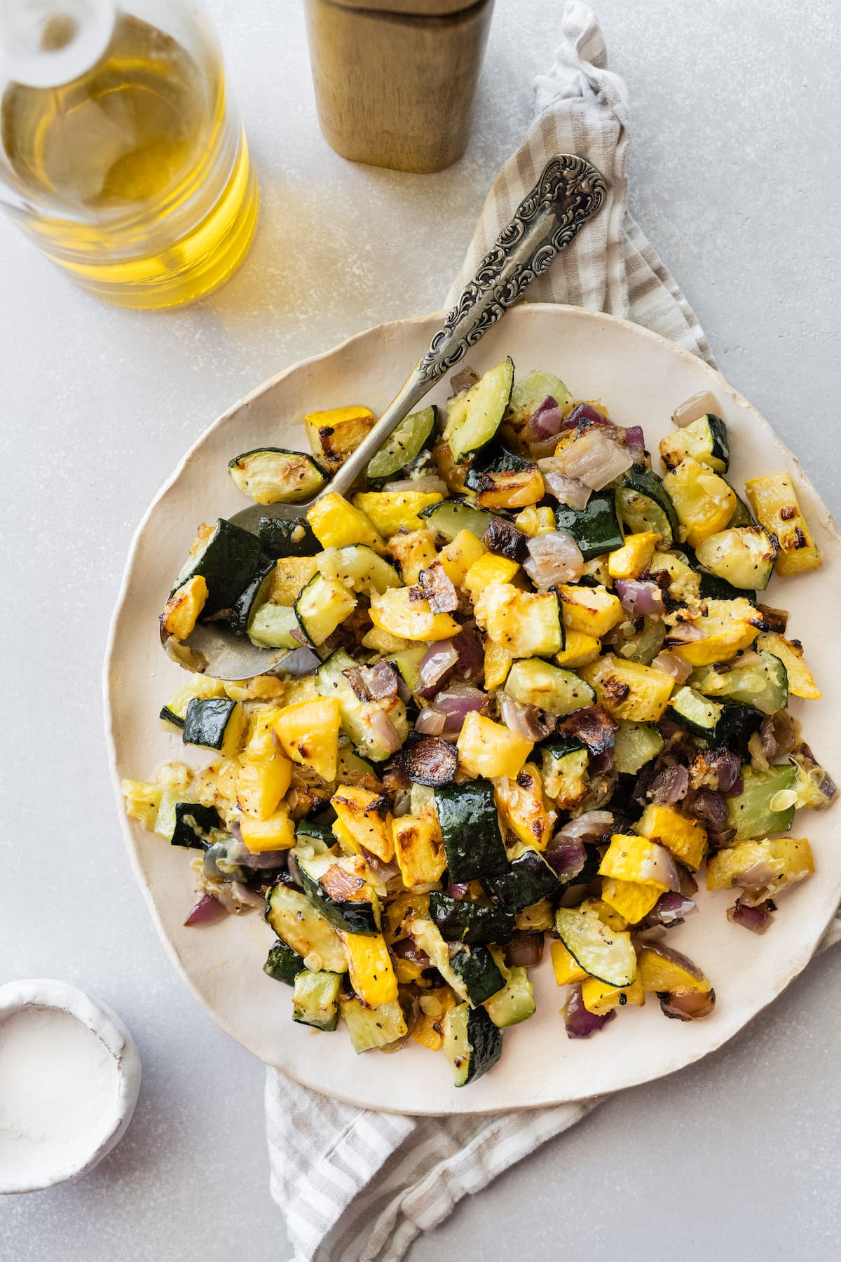 A serving of roasted zucchini and squash with salt and pepper on a plate with a metal fork.