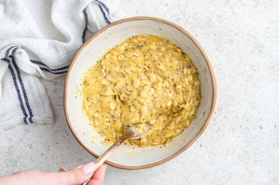 A woman's hand holds a metal fork, mixing the ingredients for the scrambled oats in a bowl.