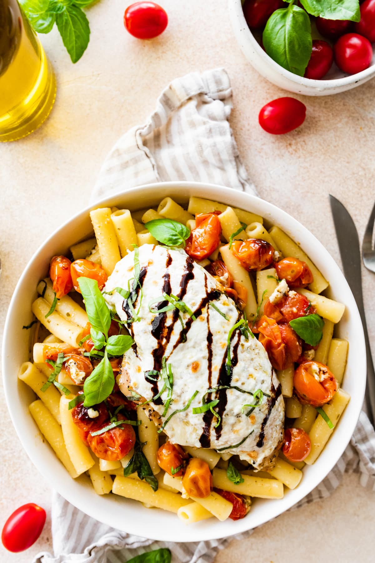 A baked caprese chicken breast with melted mozzarella and a balsamic glaze on top of a bowl of pasta.