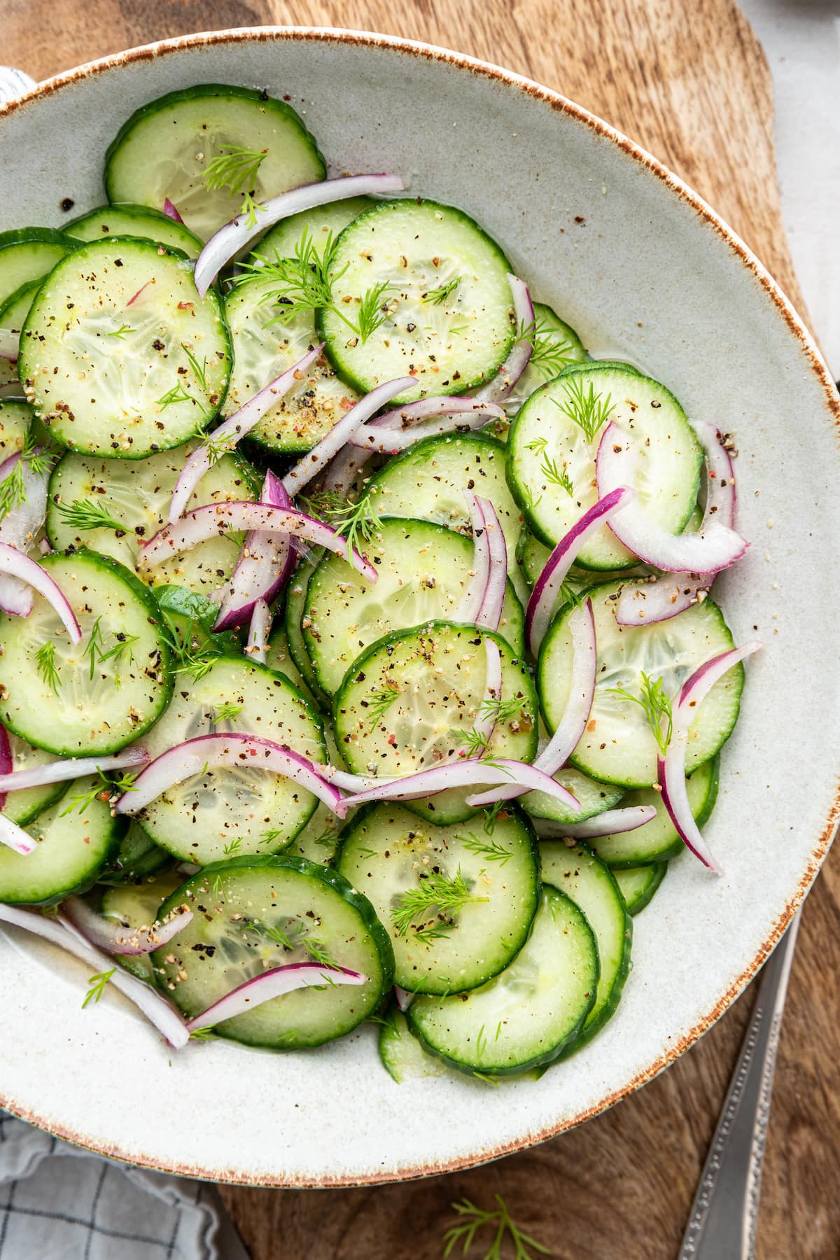 A cucumber salad with sliced red onion, dill, and ground pepper in a large bowl.