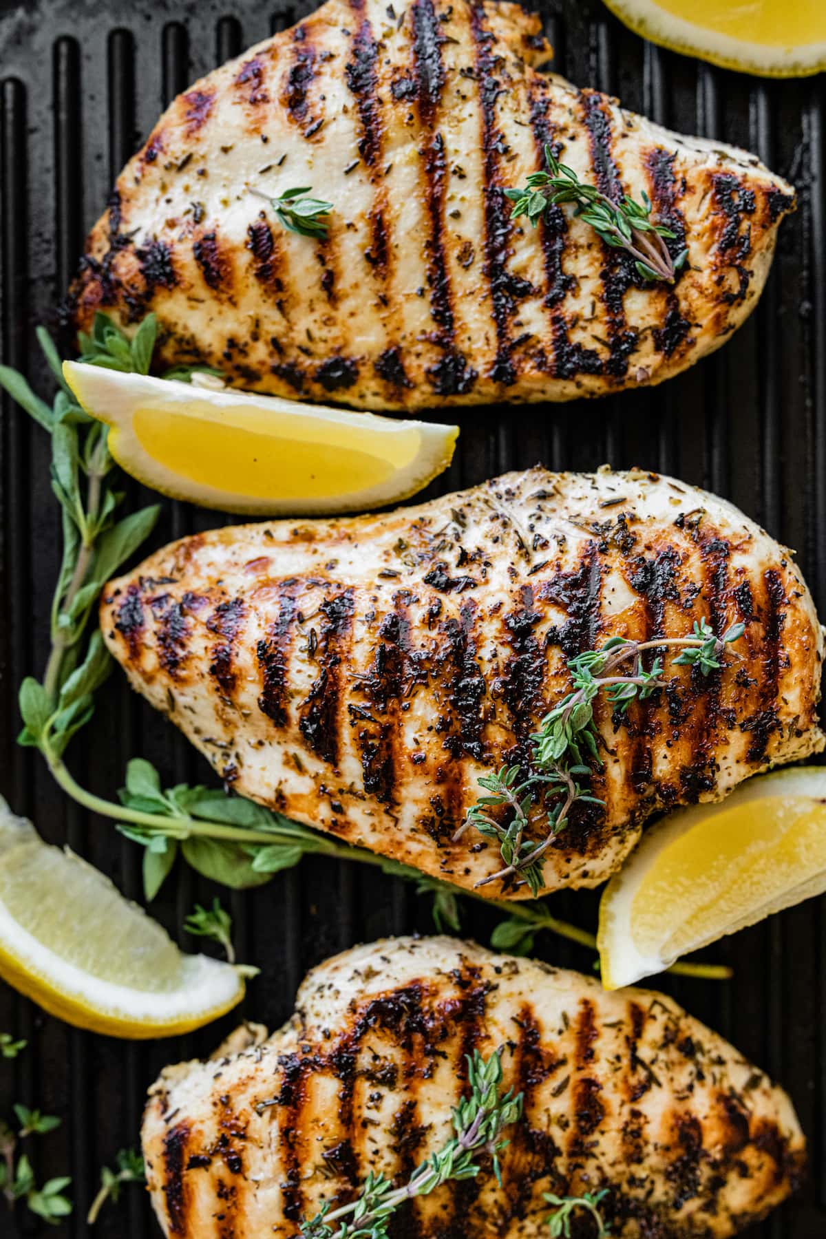 Grilled chicken breasts on a grill pan with lemon wedges.