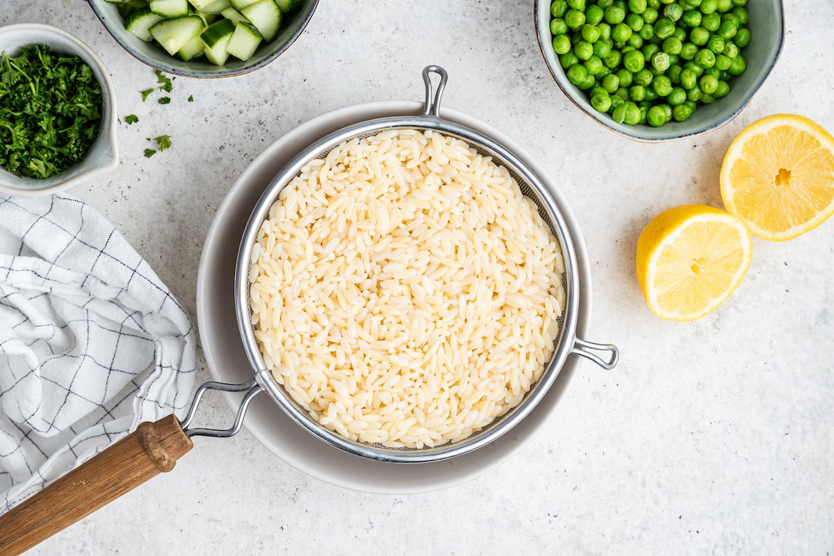 Cooked orzo pasta in a metal strainer.