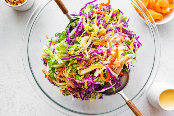 Mandarin orange chicken salad in a large glass bowl with two serving spoons.