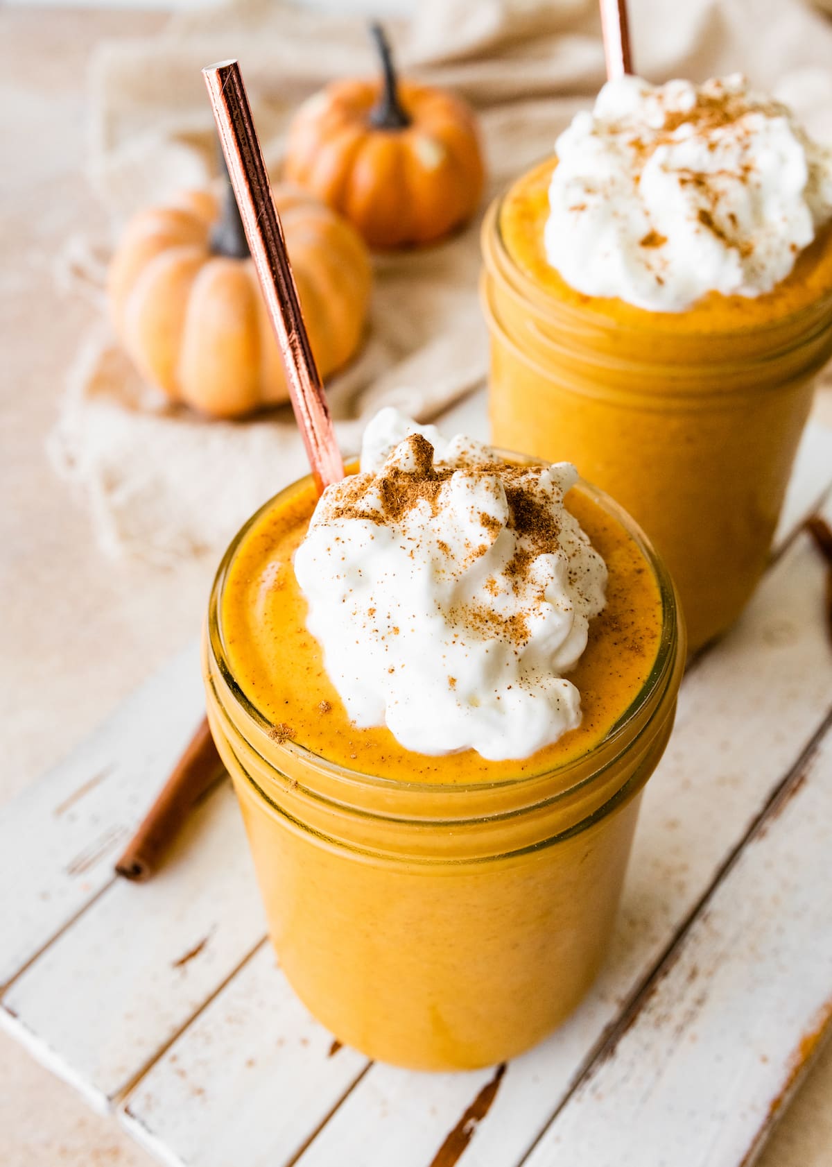 Pumpkin protein shakes served in glass mason jars, topped with whipped cream and ground cinnamon.