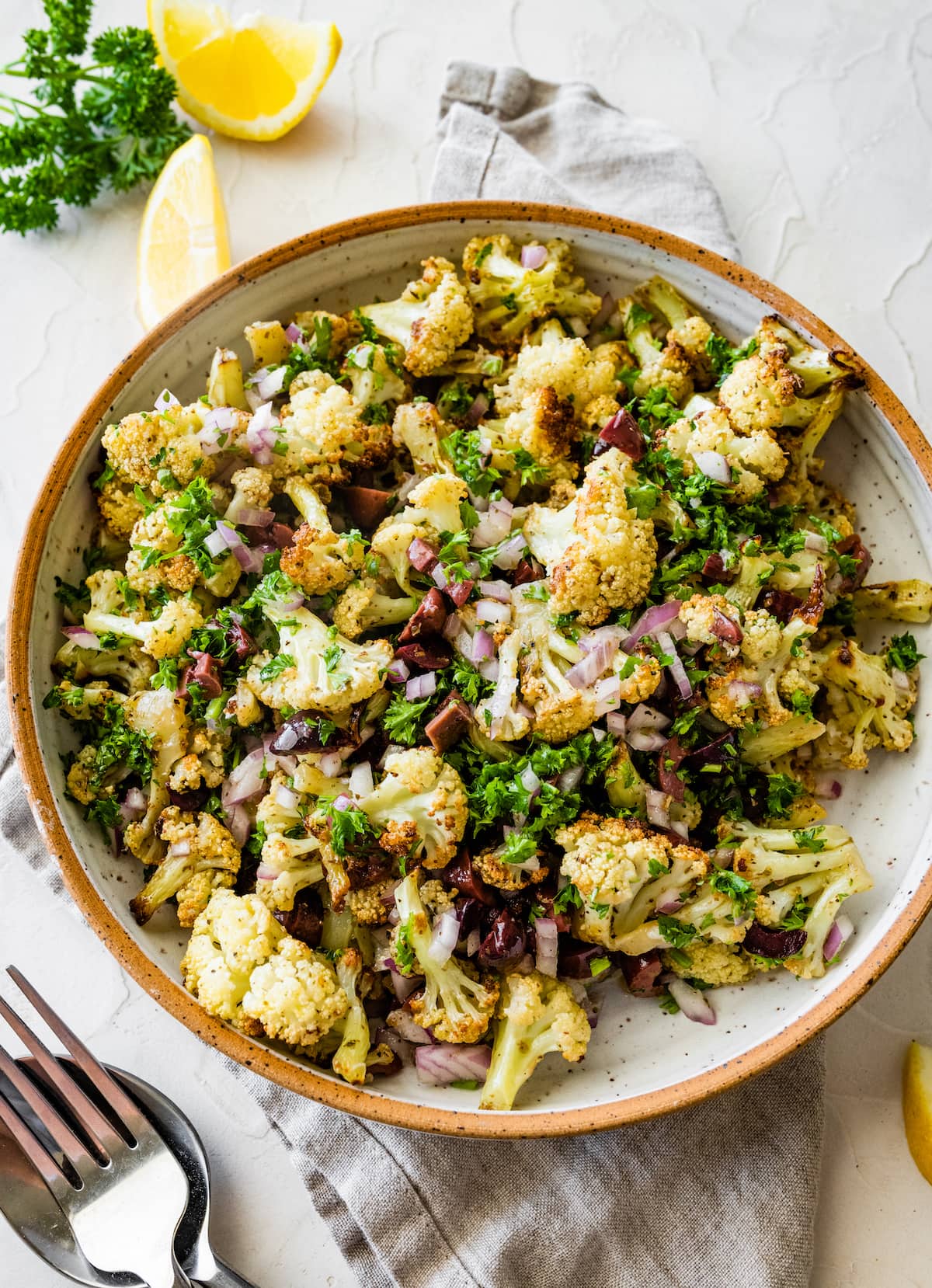 A serving of roasted cauliflower salad with olives, red onion, garlic, feta cheese, fresh herbs, and spices.