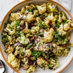 A large bowl with roasted cauliflower, olives, red onion, feta cheese, herbs, and spices.
