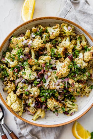 A large bowl with roasted cauliflower, olives, red onion, feta cheese, herbs, and spices.