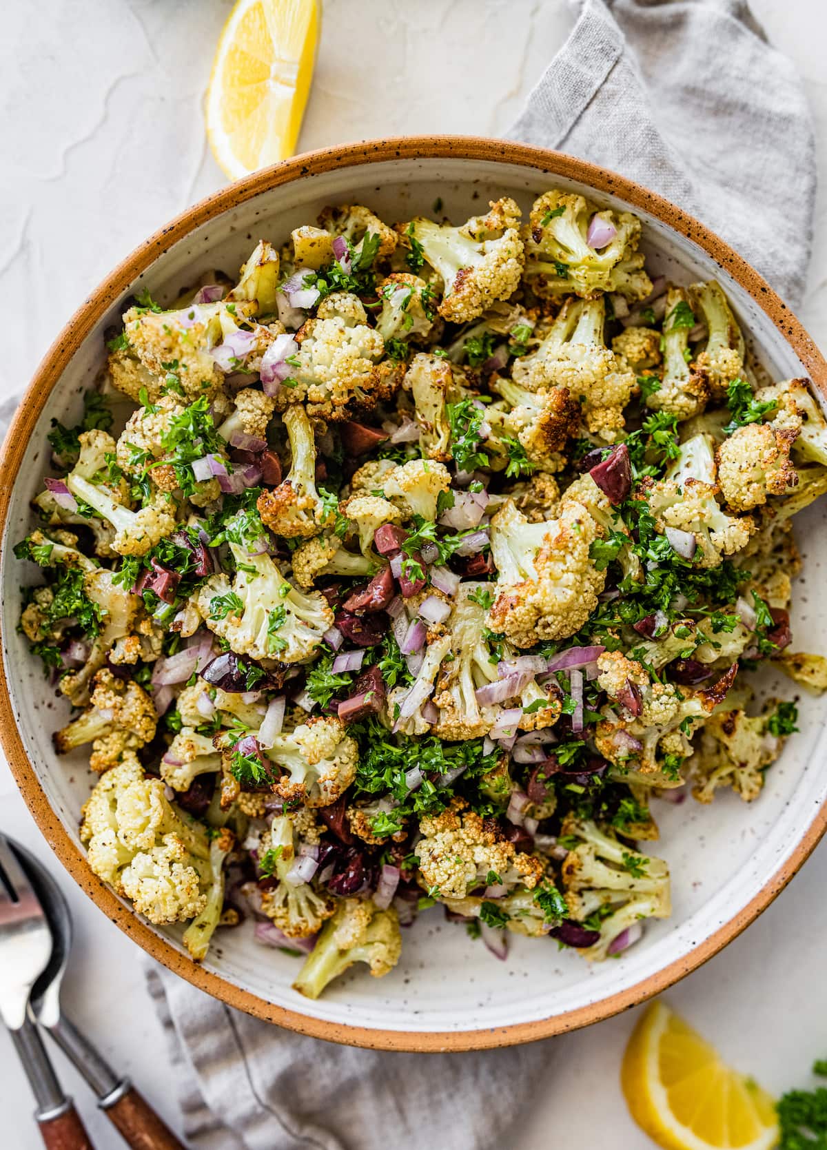 A large bowl with roasted cauliflower, olives, red onion, feta cheese, herbs, and spices.