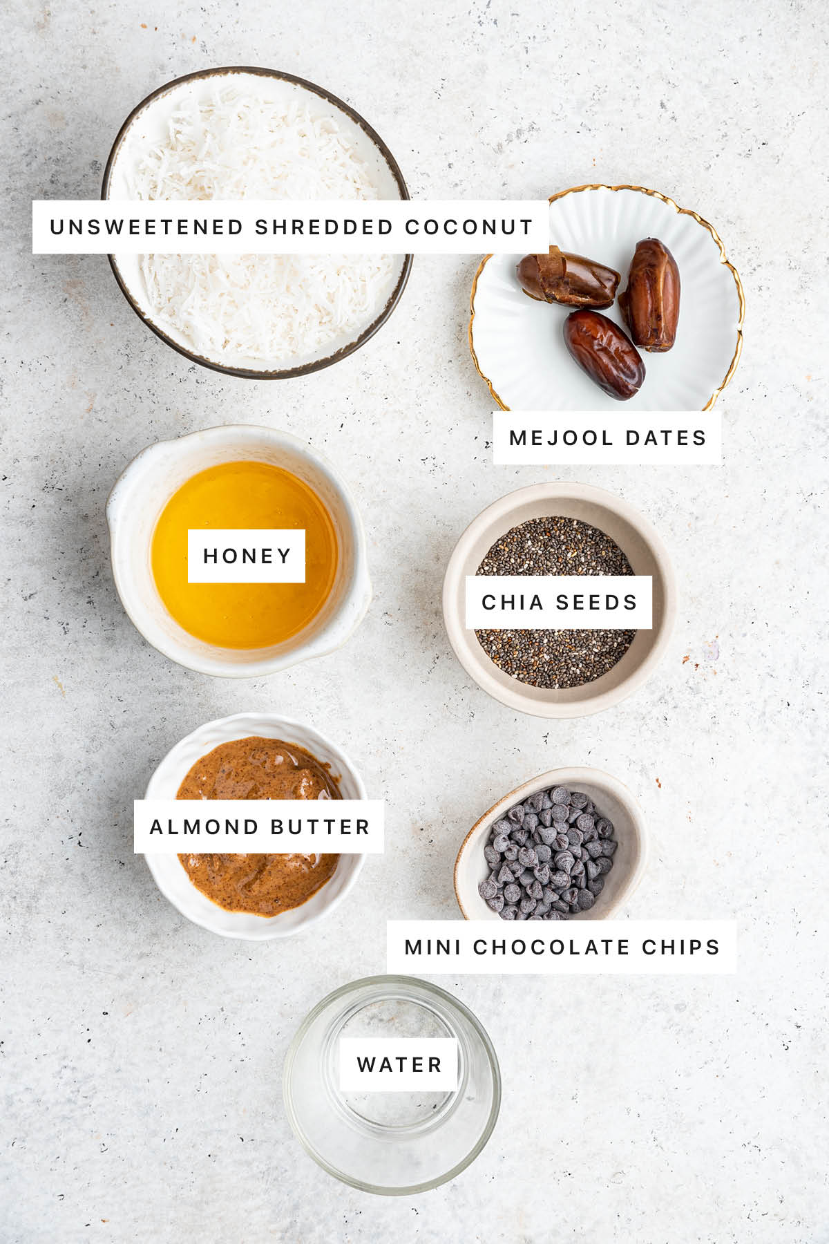 Ingredients measured out to make Coconut Chia Bars: unsweetened shredded coconut, medjool dates, honey, chia seeds, almond butter, mini chocolate chips and water.
