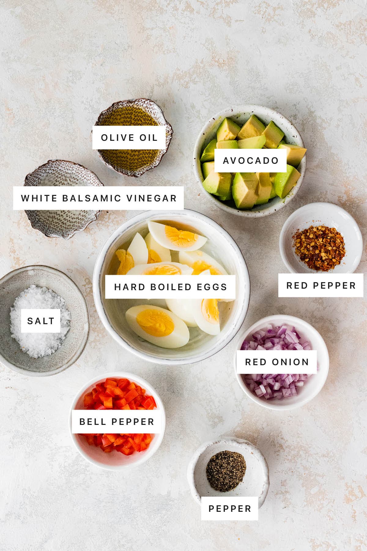 Ingredients measured out to make Hard Boiled Egg and Avocado Bowl: olive oil avocado, white balsamic vinegar, har boiled eggs, red pepper, salt, red onion, bell pepper and pepper.